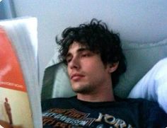 a man laying in bed next to a pillow with an orange and white book on it