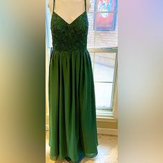 a green dress on display in front of a window with a brick wall behind it