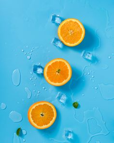 three oranges cut in half and ice cubes on a blue surface with water droplets