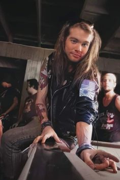 a man with long hair sitting on top of a pool table next to other people