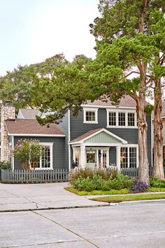 a grey house with trees and bushes in the front yard