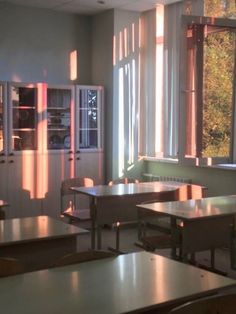 an empty classroom with desks and chairs in front of large windows that have sunlight streaming through them