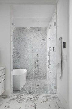 a white bathroom with marble flooring and walls, along with a walk in shower