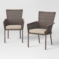 two brown wicker chairs with beige cushions on white background, one is empty and the other has an off - white cushion