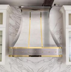 a stainless steel range hood mounted on the wall in a kitchen with white cabinets and marble countertops