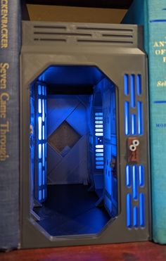 the inside of a computer case with blue light coming from it's door and books behind it