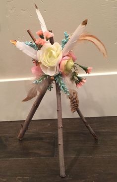 an arrangement of feathers and flowers on top of a wooden stand