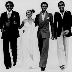 an old black and white photo of three men and a woman in formal wear standing next to each other