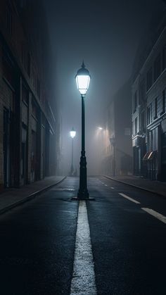 a street light on a foggy night in the middle of an empty city road