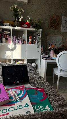 a laptop computer sitting on top of a bed next to two books and a white chair