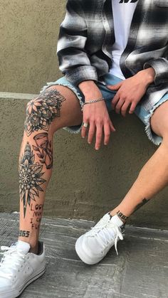 a person sitting on the ground with their legs crossed and tattoos on his leg,