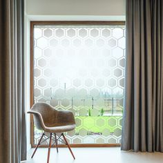 a chair sitting in front of a window with curtains on the outside and an open window behind it