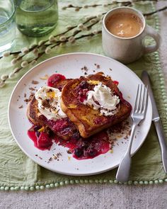 a white plate topped with french toast covered in berries and whipped cream next to a cup of coffee