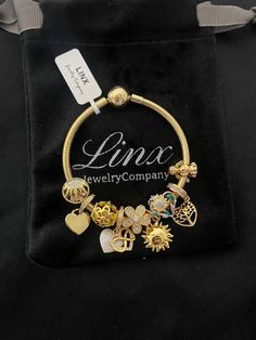 a gold bracelet with charms on it sitting in a black velvet bag that says linx jewelry company