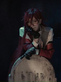 a woman with red hair and glasses sitting on top of a large stone statue in the dark