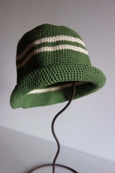 a green crocheted hat with white stripes on the brim sits on a table