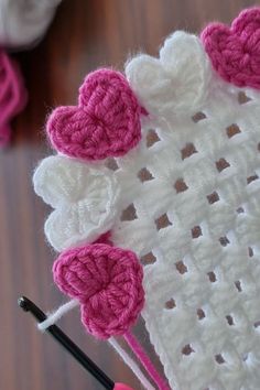 a crocheted blanket with pink and white hearts on it, next to two knitting needles