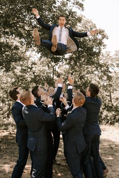 a group of men in suits and ties are holding up a man with his feet in the air