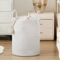 a large white basket sitting on top of a wooden floor next to a lamp and dresser