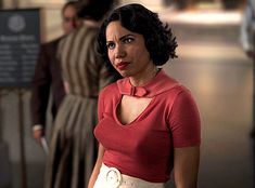 a woman in a red shirt and white skirt standing next to other people at an airport