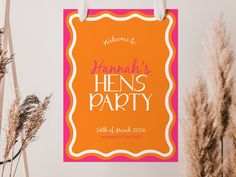 an orange and pink hens party sign hanging on a wall next to dried flowers