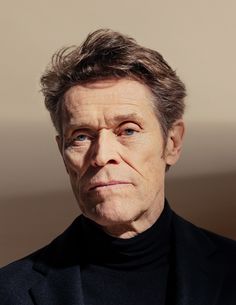 an older man wearing a black turtle neck sweater looks into the distance with his eyes wide open