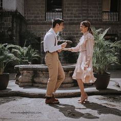 a man and woman are dancing together in front of a fountain with plants behind them