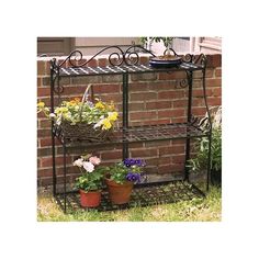 an iron shelf with potted plants and flowers on it in front of a brick wall