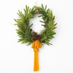 a christmas wreath with pine cones and yellow ribbon hanging on a wall ornament