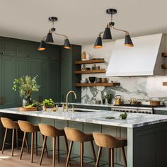 a kitchen with green cabinets, marble counter tops and bar stools in the center