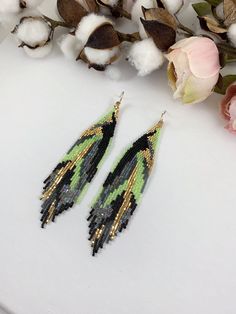 two pairs of black, green and gold beaded earrings on top of cotton flowers