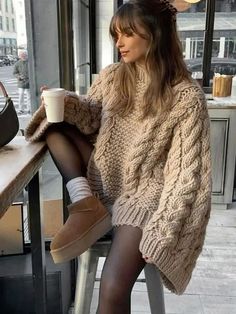 a woman sitting at a table with her legs crossed and holding a cup in front of her