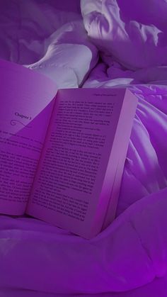 an open book sitting on top of a bed under a purple comforter with sheets