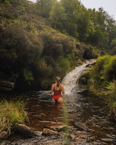 a woman in a red bathing suit wading through a stream