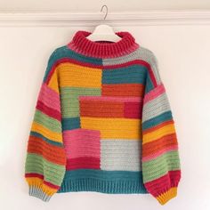 a multicolored sweater hanging on a hanger against a pink wall with a white background