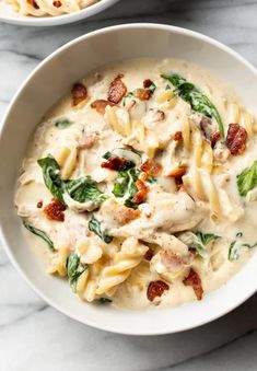 two white bowls filled with pasta and spinach covered in sauce on top of a marble counter