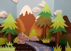 a paper cut out of trees and mountains with a river running through it, surrounded by grass and rocks