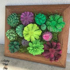 a wooden frame filled with fake flowers and greenery in the shape of succulents