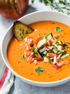 a white bowl filled with carrot soup and garnished with cucumber slices