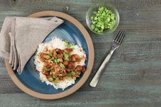 a blue plate topped with rice and meat next to a bowl of chopped green onions