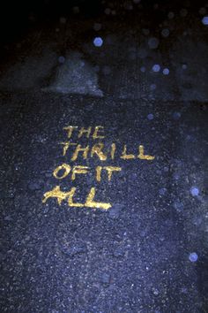 the word'the thrill of it all'written in yellow chalk on a sidewalk