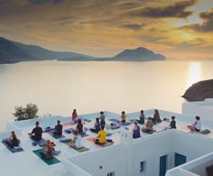 a group of people doing yoga on top of a building next to the ocean at sunset