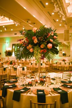 a tall vase filled with flowers and greenery on top of a round dining table