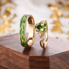 two gold rings with green and yellow stones on top of a wooden stand next to each other