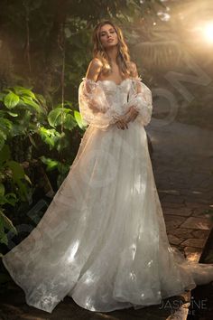 a woman in a white wedding dress standing on a path with trees and bushes behind her