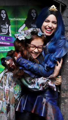 two women hugging each other in front of a wall with an ad on the side