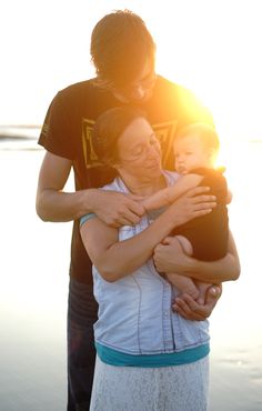 a woman holding a child in her arms while standing next to two other people on the beach