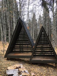 two triangular wooden structures sitting in the middle of a forest with fallen leaves on the ground