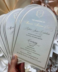 the wedding program is being held up in front of some white flowers and paper fans