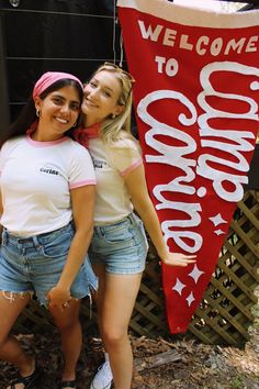 two girls standing next to each other in front of a welcome sign